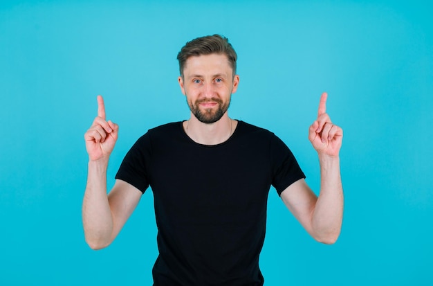 Junger Mann zeigt mit Zeigefingern auf blauem Hintergrund nach oben