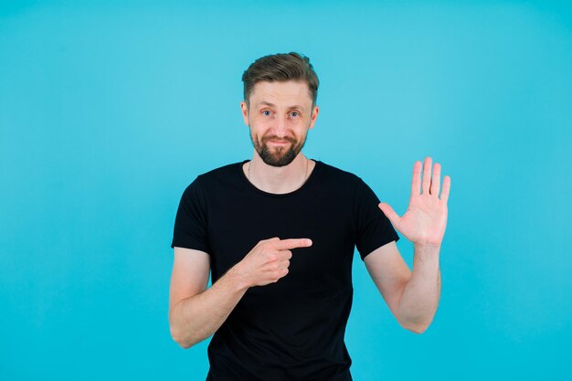 Junger Mann zeigt seine Handvoll mit Zeigefinger auf blauem Hintergrund
