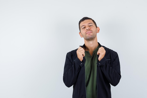 Junger Mann zieht Kragen seiner Jacke in T-Shirt, Jacke und sieht cool aus. Vorderansicht.