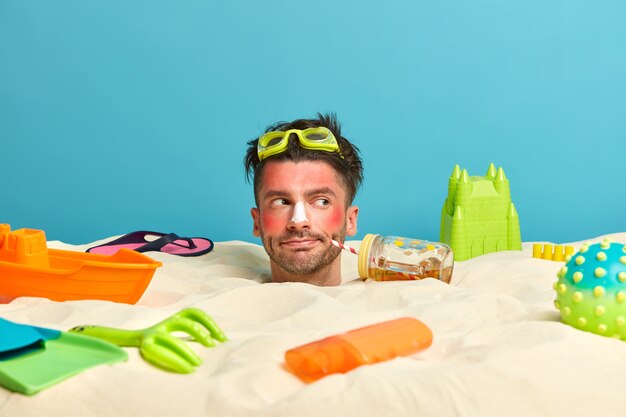 Kostenloses Foto junger mannkopf mit sonnenschutzcreme auf gesicht umgeben von strandaccessoires