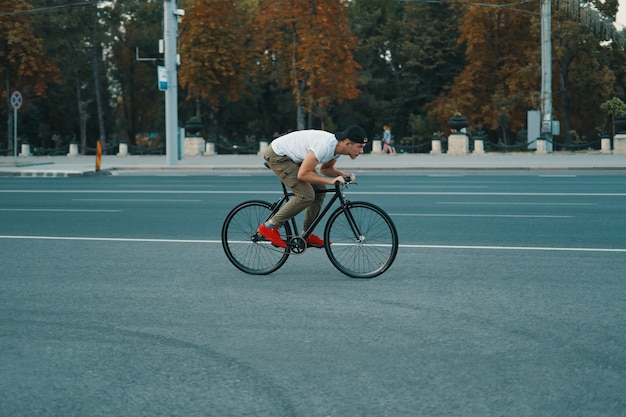 Junger moderner Mann, der auf einem klassischen Fahrrad auf der Stadtstraße radelt