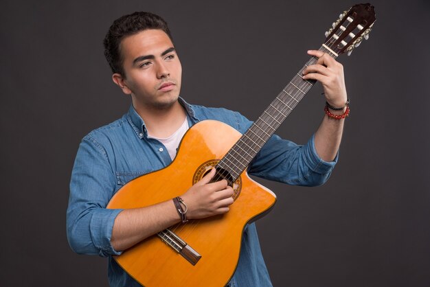 Junger Musiker, der eine schöne Gitarre auf schwarzem Hintergrund hält. Hochwertiges Foto