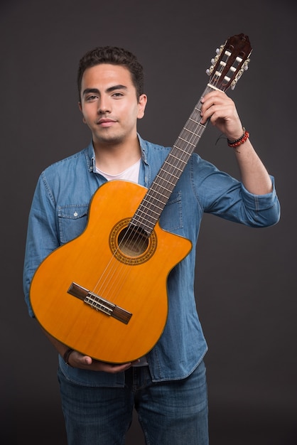Junger Musiker, der Gitarre auf schwarzem Hintergrund hält