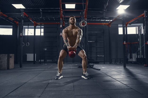 Junger muskulöser Athlet, der Kniebeugen im Fitnessstudio mit dem Gewicht übt