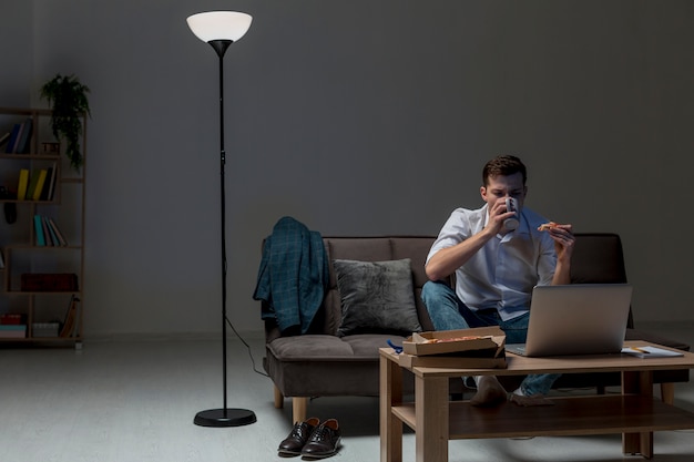 Junger Profi, der einen Snack während der Arbeit von zu Hause aus hat