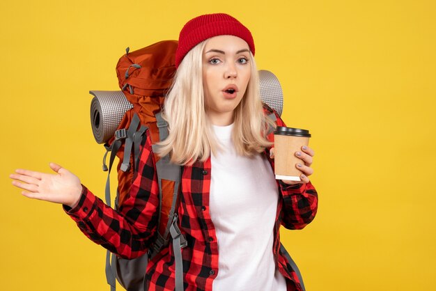 Junger Reisender der Vorderansicht mit ihrem Rucksack, der Kaffeetasse hält auf gelber Wand hält