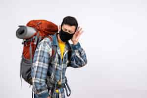Kostenloses Foto junger reisender der vorderansicht mit rucksack und maske, die auf etwas hören