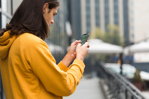 Junger Reisender mit dem langen Haar sein Telefon überprüfend