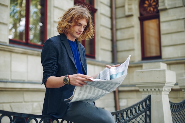 Junger rötlicher mann, der zeitung nahe altem artgebäude liest