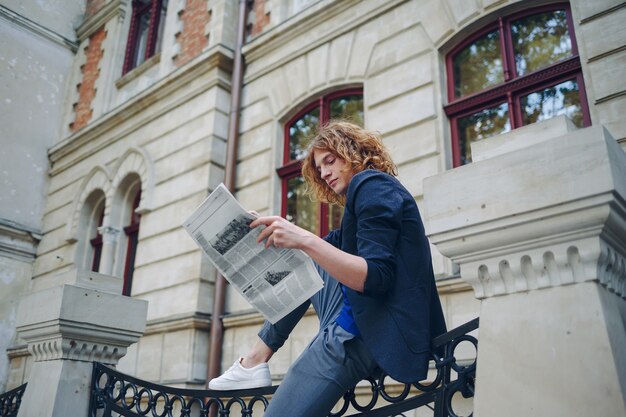 Junger rötlicher Mann, der Zeitung nahe altem Artgebäude liest