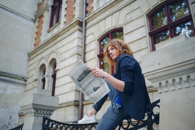 Junger rötlicher Mann, der Zeitung nahe altem Artgebäude liest