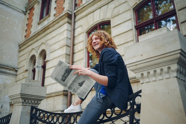 Junger rötlicher Mann, der Zeitung nahe altem Artgebäude liest