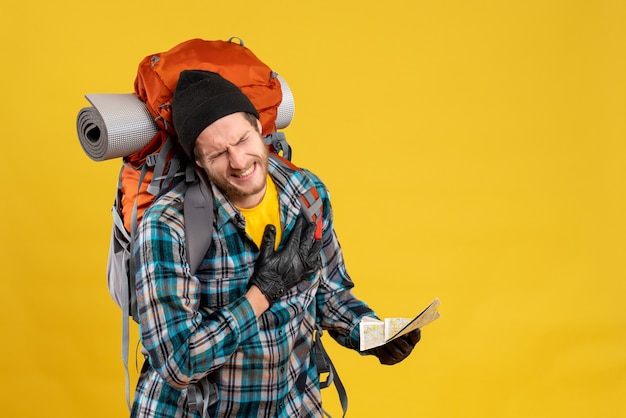 junger Rucksacktourist mit schwarzem Hut, der eine Reisekarte hält und sein Herz mit Schmerzen