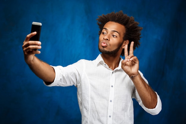 Junger schöner afrikanischer Mann, der selfie über blaue Wand macht.