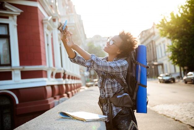 Kostenloses Foto junger schöner afrikanischer weiblicher reisender mit dem lächelnden rucksack, der selfie macht.