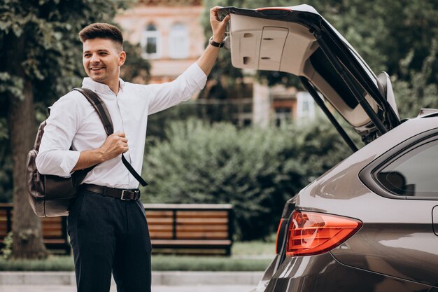 Junger schöner Geschäftsmann, der durch Auto mit Reisetasche steht