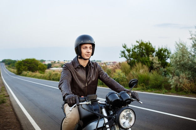 Junger schöner Mann, der auf Motorrad an Landstraße reitet.