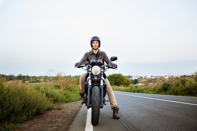 Junger schöner Mann, der auf Motorrad an Landstraße reitet.