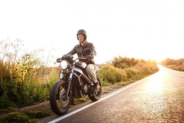 Junger schöner Mann, der auf Motorrad an Landstraße reitet.