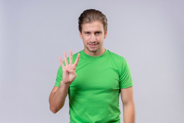 Junger schöner Mann, der grünes T-Shirt trägt, das mit den Fingern Nummer drei zeigt und zeigt