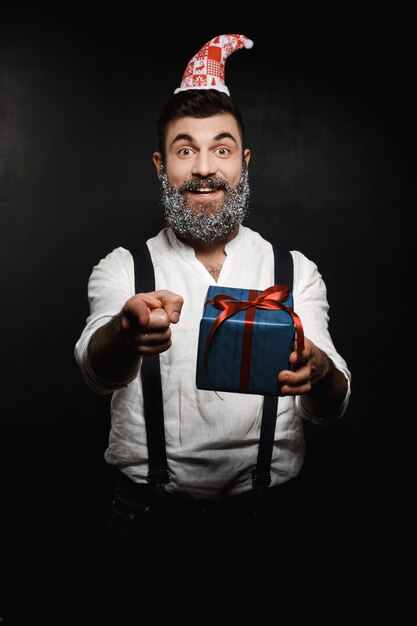 Kostenloses Foto junger schöner mann, der weihnachtsgeschenkbox zeigt finger zeigt.