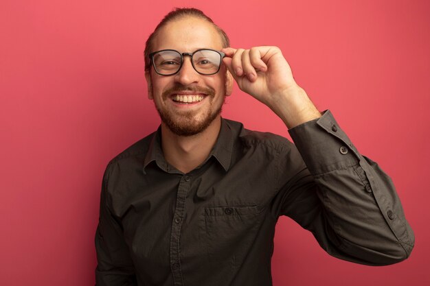 Junger schöner Mann im grauen Hemd und in den Gläsern, die mit glücklichem Gesicht lächeln