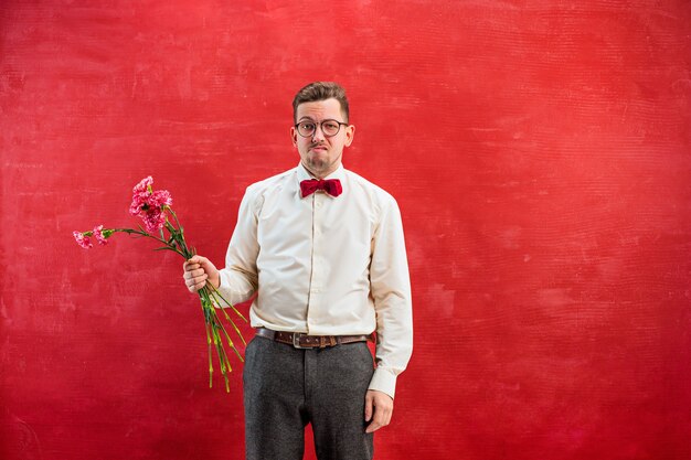 Junger schöner Mann mit Blumen auf rotem Studiohintergrund