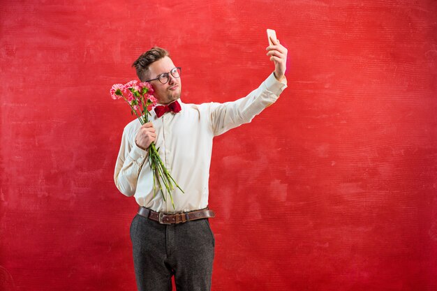 Junger schöner Mann mit Blumen und Telefon