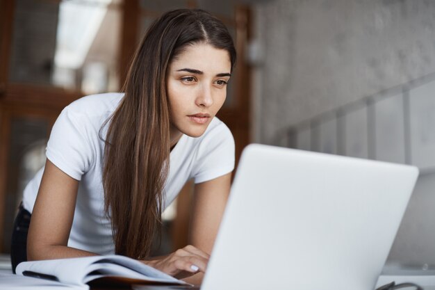 Junger schöner Student, der Internet auf einem Laptop-Computer sucht, der nach neuen Informationen auf Universitätsbibliothek sucht.