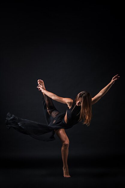 Junger schöner Tänzer im beige Kleid, das auf schwarzem Hintergrund tanzt
