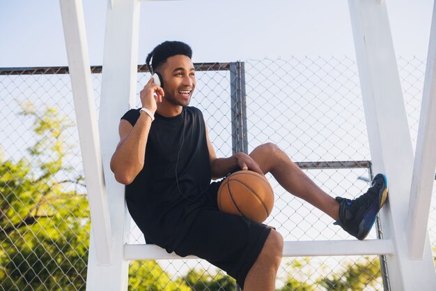 Junger schwarzer Mann, der Sport macht, Basketball, aktiven Lebensstil, Sommermorgen spielt, glücklich lächelt, Spaß hat, Musik auf Kopfhörern zu hören