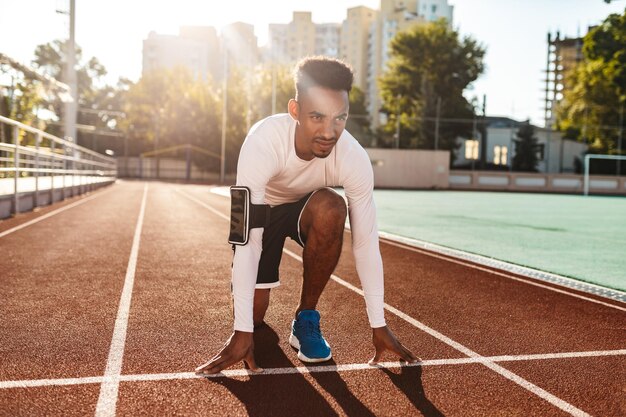 Junger selbstbewusster afroamerikanischer Sportler bereitet sich auf das Laufen auf der Rennstrecke im Stadtstadion vor