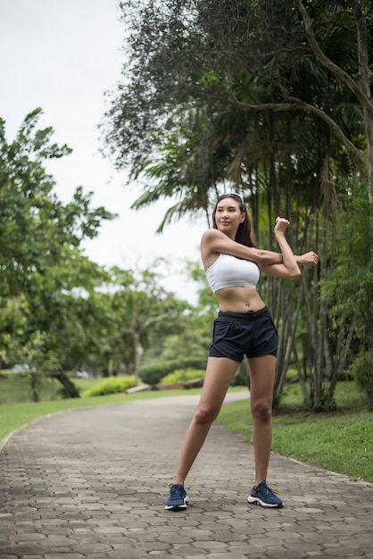 Junger Sportfrauenläufer, der Körper vor Lauf auf Bahn im Park ausdehnt.