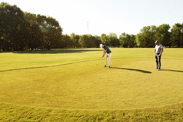 Junger Sportler, der mit seinem Lehrer Golf übt