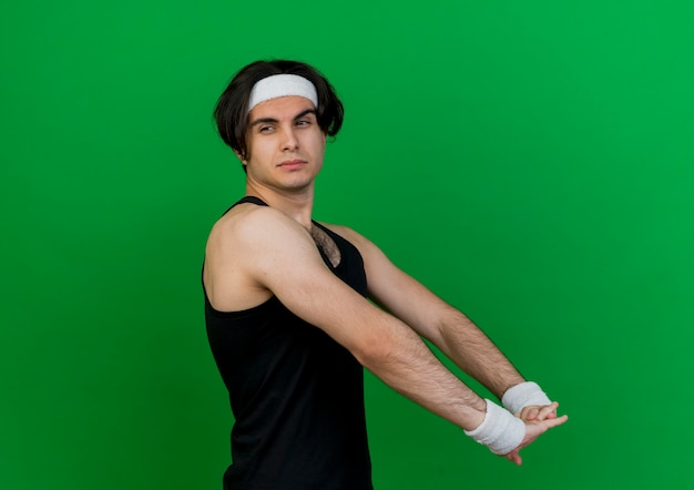 Junger sportlicher Mann, der Sportbekleidung und Stirnband trägt, die seine Hände strecken