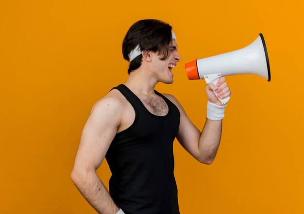 Junger sportlicher Mann, der Sportbekleidung und Stirnband trägt, die zum Megaphon schreien