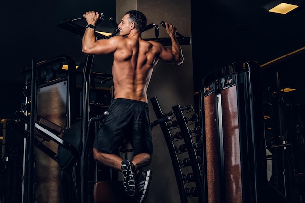 Junger sportlicher Mann macht Übungen für seinen Rücken im dunklen Fitnessstudio.