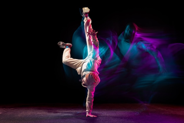 Junger sportlicher Mann tanzt Breakdance isoliert über schwarzem Hintergrund in Neon mit gemischten Lichtern