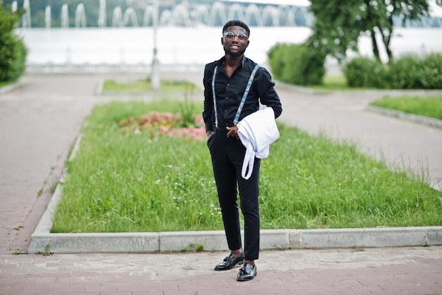 Junger stilvoller afrikanisch-amerikanischer männlicher Arzt hält weißen Mantel zur Hand und posiert im Freien