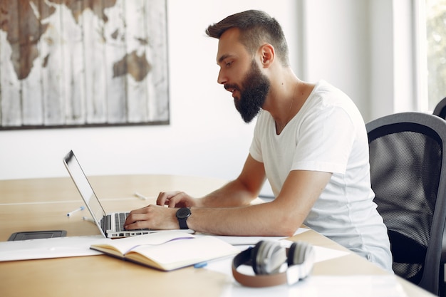 Junger Student, der am Tisch sitzt und den Laptop benutzt