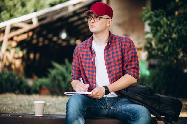 Junger Student, der an einem Computer außerhalb des Cafés im Park arbeitet