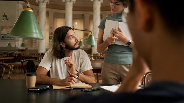 Junger Student, der mit Tutor in der Bibliothek studiert Universitätsstudenten sitzen zusammen und lesen Bücher Junge Menschen bereiten sich auf Prüfungen in der College-Bibliothek vor