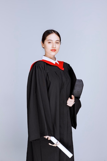 Junger Student mit Kleid und Diplom posiert für den Abschlusstag. Foto in hoher Qualität