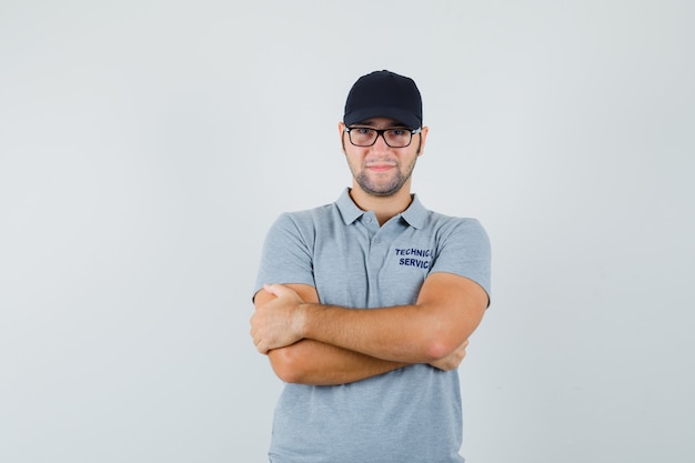 Junger Techniker, der mit verschränkten Armen in der grauen Uniform steht und selbstbewusst aussieht.