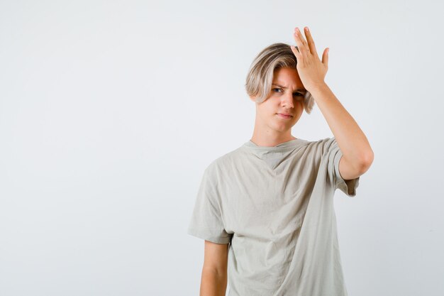 Junger Teenager, der die Hand im T-Shirt auf dem Kopf hält und vergesslich aussieht. Vorderansicht.