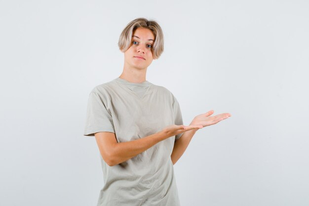 Junger Teenager, der eine einladende Geste im T-Shirt zeigt und sanft aussieht. Vorderansicht.