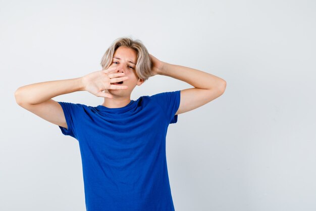 Junger Teenager, der im blauen T-Shirt gähnt und sich ausdehnt und schläfrig aussieht. Vorderansicht.