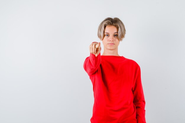 Junger Teenager, der im roten Pullover nach vorne zeigt und ernst aussieht. Vorderansicht.