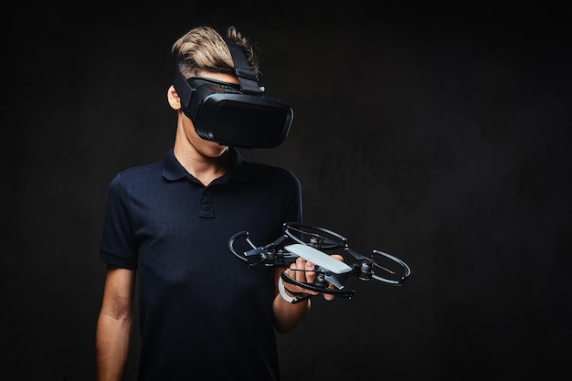 Junger Teenager in einem schwarzen T-Shirt trägt eine Virtual-Reality-Brille und hält einen Quadrocopter. Auf dem dunklen Hintergrund isoliert.
