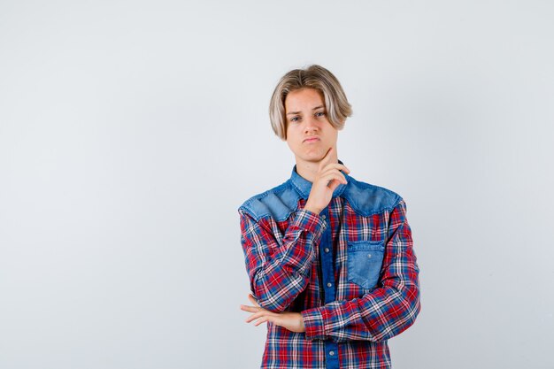 Junger Teenager in kariertem Hemd, der den Kiefer mit dem Finger berührt und nachdenklich aussieht